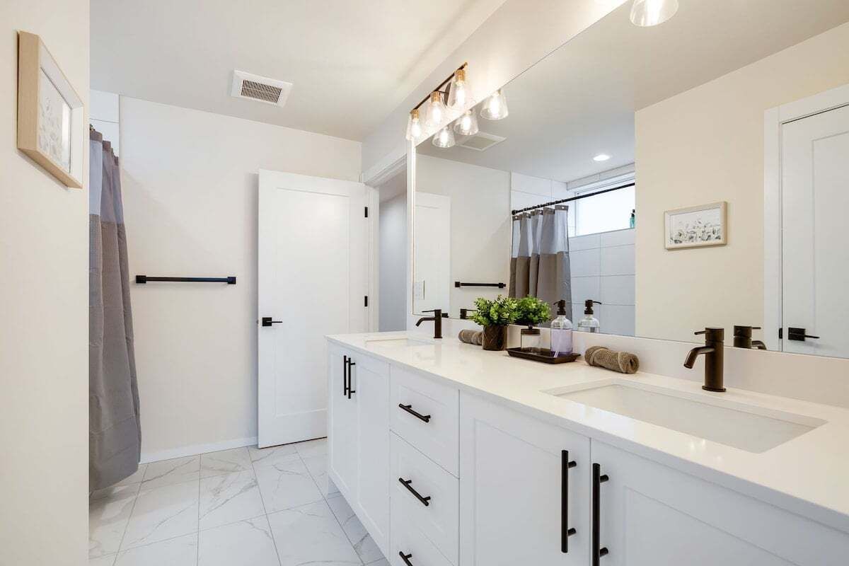 A modern bathroom with a large mirror, white cabinets, and a countertop with toiletries.