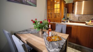 A dining table with a vase of red roses, a bottle, and two glasses on a tray, set in a kitchen with wooden cabinets and a painting on the wall. - Sea View Nikos Apartment (Ναύπλιο)