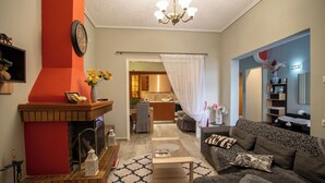 A living room with a fireplace, a sofa, a coffee table, and a kitchen in the background. - Sea View Nikos Apartment (Ναύπλιο)