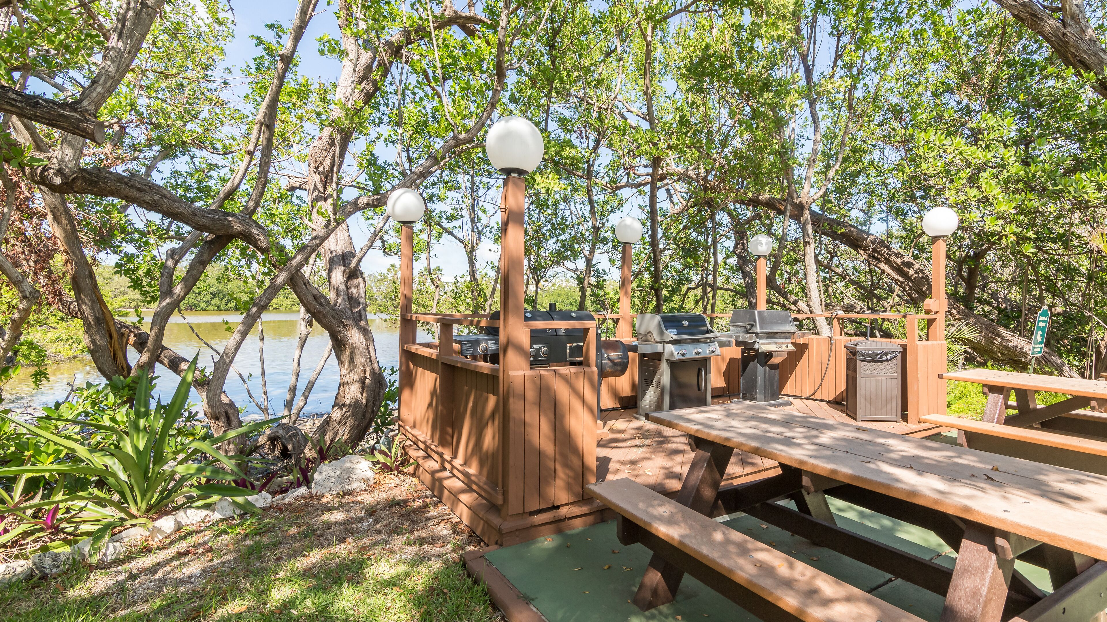 A wooden deck with picnic tables and a barbecue grill area overlooking a lake.