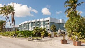 Een meerhoog hotel met een plat dak, omringd door palmbomen en begroeiing.