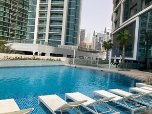 Una piscina con sillas de descanso y edificios modernos al fondo.