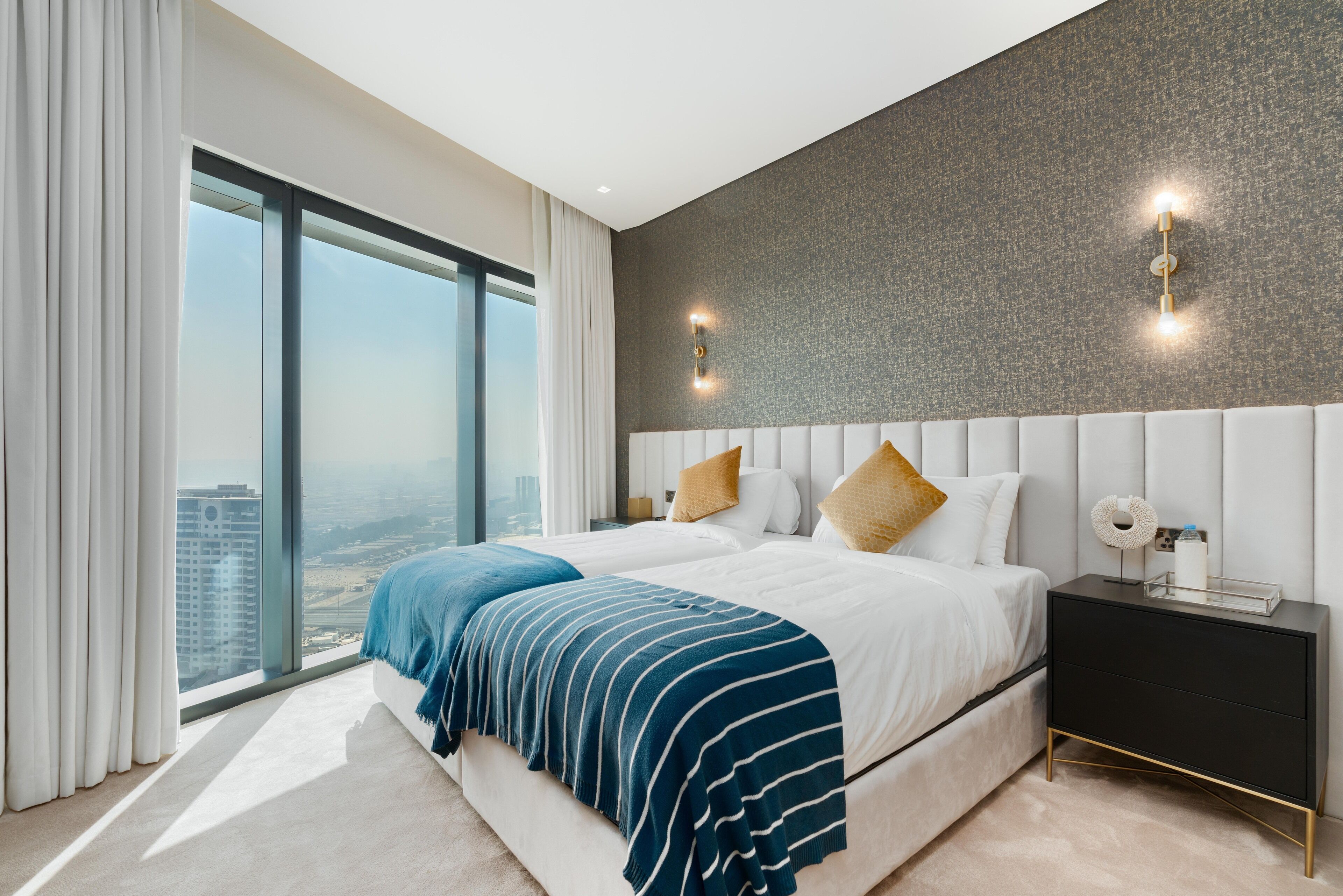 A modern bedroom with a large bed, a nightstand, and a view of the city.
