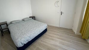 Un dormitorio con cama, una mesita de noche, una puerta decorada con una luna creciente y una pequeña mesa.