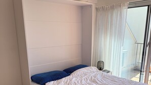 Ein Schlafzimmer mit Bett, einem kleinen Tisch, einer Klimaanlage und Blick auf den Balkon.