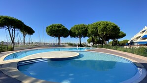 Ein Pool mit geschwungener Form, umgeben von einer gefliesten Terrasse und Bäumen.