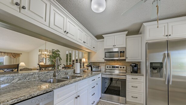 A modern kitchen with white cabinets, granite countertops, stainless steel appliances, and a chandelier. - Condo in Golf Community (Naples)