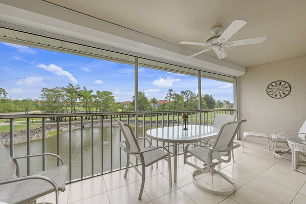Un balcon donnant sur un terrain de golf, un ventilateur de plafond et une table ronde avec des chaises.
