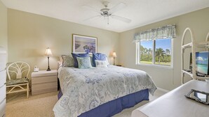 A bedroom with a bed, nightstands, a chair, a desk, a ceiling fan, a window with a view, and a framed picture on the wall. - Condo in Golf Community (Naples)