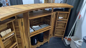 Un meuble de rangement en bois, doté d’étagères et de compartiments, comprenant une section avec des serviettes pliées et une étagère contenant des produits de nettoyage.