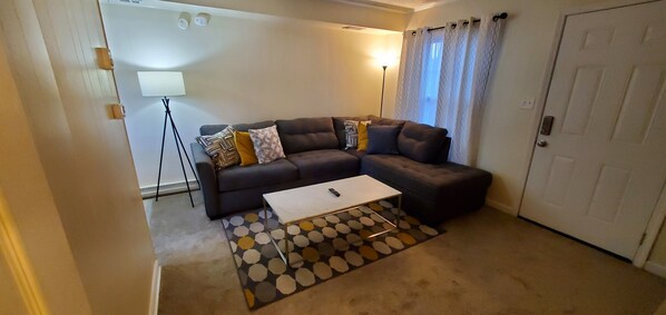 A living room with a sectional sofa, a coffee table, a floor lamp, and a patterned rug.