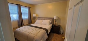 A hotel room with a bed, two bedside lamps, a nightstand, and a window with curtains.