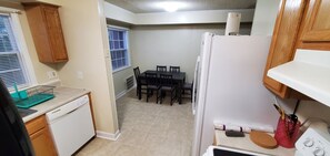 A compact kitchen with a dishwasher, a refrigerator, a dining table with chairs, and wooden cabinets.