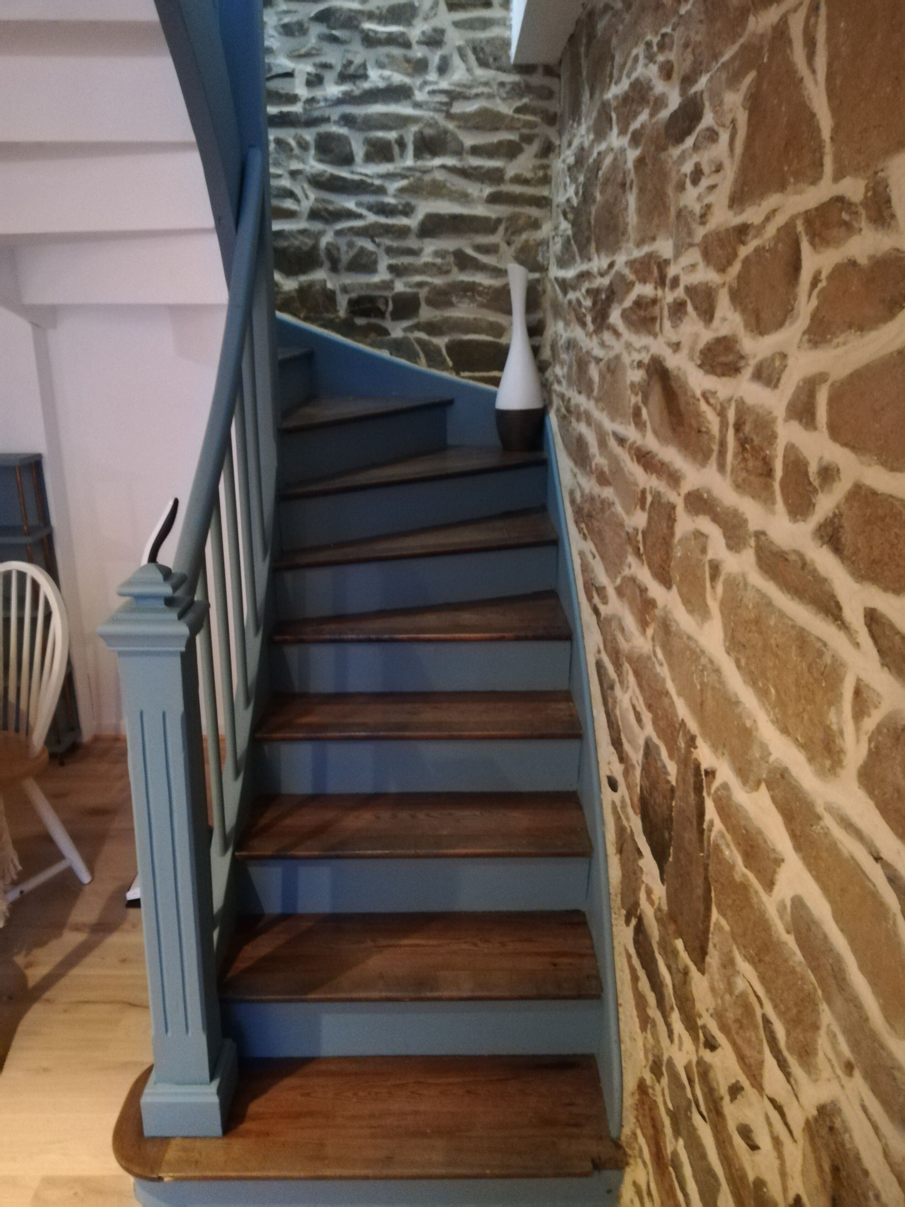 Un escalier avec des rampes bleues et des marches en bois menant à un mur de pierre.