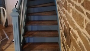 Eine Treppe mit blauen Geländern und Holzstufen, die zu einer Steinmauer hinaufführt.