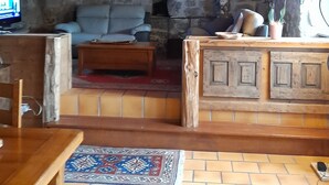 A rustic room with a stone wall, wooden ceiling beams, a television, a sofa, a coffee table, and a patterned rug. - 1802 Auvergne house (Saint-Donat)