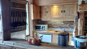 A rustic kitchen with wooden cabinets, a microwave, a sink, and a large pot on the counter. - 1802 Auvergne house (Saint-Donat)