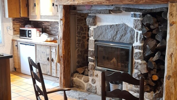 A cozy room with a stone fireplace, wooden ceiling beams, and a kitchen area with a microwave and cabinets. - 1802 Auvergne house (Saint-Donat)