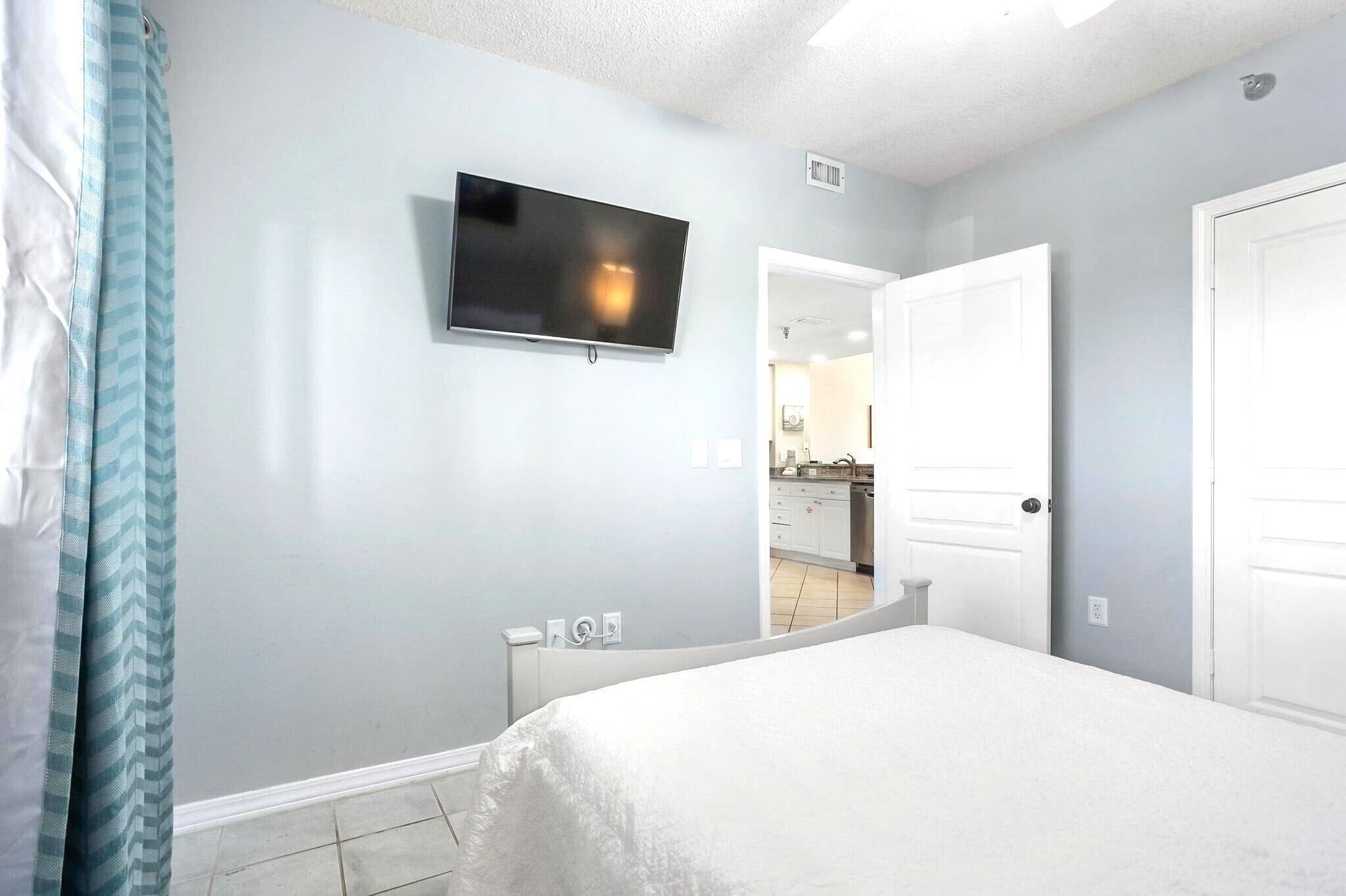 A bedroom with a bed, a television mounted on the wall, and a bathroom visible through an open door.