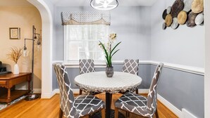 Un comedor con una mesa redonda, sillas estampadas, un florero con flores, una lámpara colgante y una pared decorada con platos.