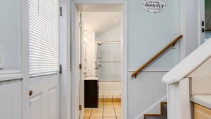 Un pasillo con una puerta que da a un baño, un cartel que indica servicios de lavandería y una escalera.