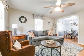 A living room with a gray sofa, a brown leather armchair, a coffee table, a side table with a lamp, and a ceiling fan.