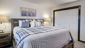 A bedroom with a large bed, two bedside tables, a headboard, a wall-mounted painting, and a closet with a sliding door. - CK Stay Hotel (Butte)