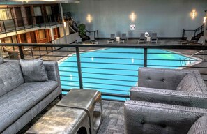 A pool area with lounge chairs and a sofa, a staircase, and a view of the building's interior.