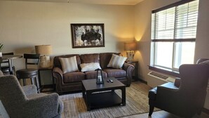 A living room with a brown leather sofa, two armchairs, a coffee table, and a lamp. - CK Stay Hotel (Butte)