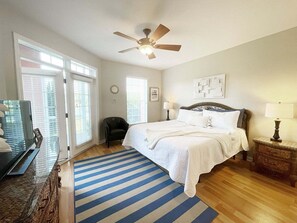 A bedroom with a bed, a ceiling fan, a window with blinds, a chair, and a TV. - Seaside at Anastasia B102 (St. Augustine)