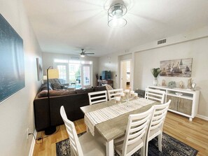 A modern living room with a sofa, dining table, and chairs. There is a ceiling fan and a TV in the background. - Seaside at Anastasia B102 (St. Augustine)