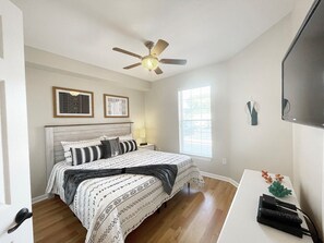 Ein Schlafzimmer mit Bett, Deckenventilator, Fenster und Fernseher.