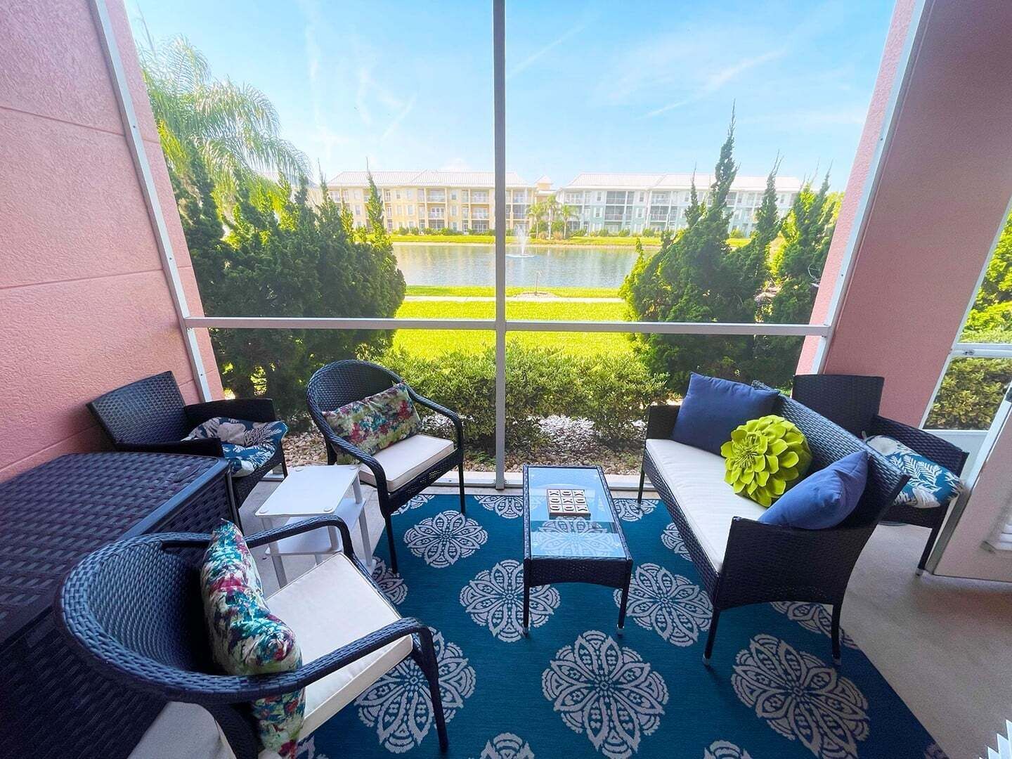 A balcony with wicker furniture, a patterned rug, and a view of a building and greenery.