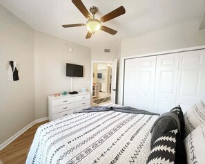 A bedroom with a bed, a ceiling fan, a TV, a dresser, and a wardrobe. - Seaside at Anastasia B102 (St. Augustine)