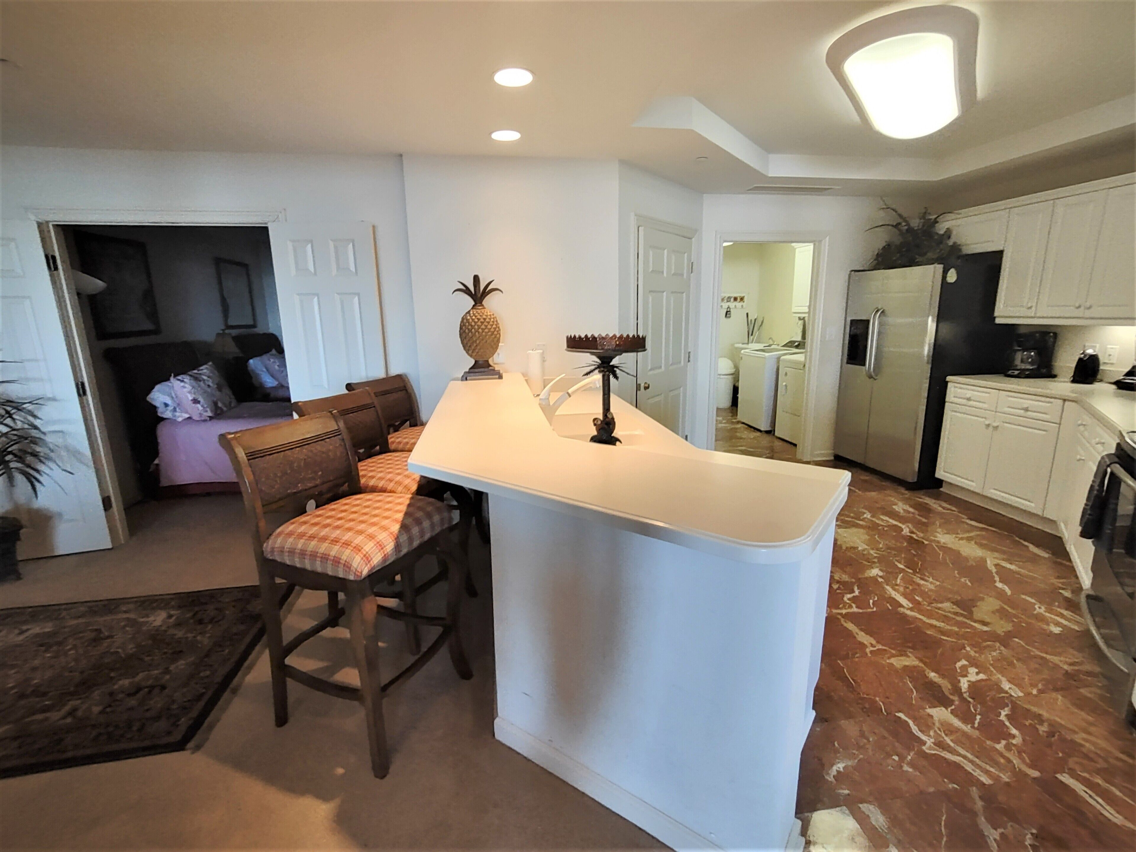 A modern kitchen with white cabinets, a marble floor, and a breakfast bar with chairs.
