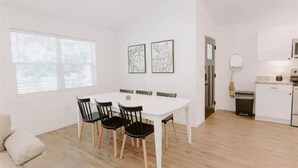 Une cuisine moderne avec des armoires blanches, un plan de travail blanc et un four encastré. On y trouve également un coin repas avec une table blanche et des chaises noires.