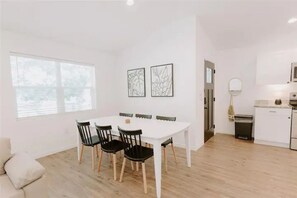 A modern kitchen with white cabinets, a white countertop, and a built-in oven. There is a dining area with a white table and black chairs.