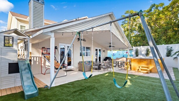 Ein Garten mit Schaukel, Rutsche, überdachter Terrasse und Grillplatz.