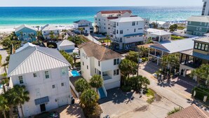 Un quartier résidentiel en bord de mer, avec de nombreuses maisons à deux étages, une piscine bien visible et une plage en arrière-plan.
