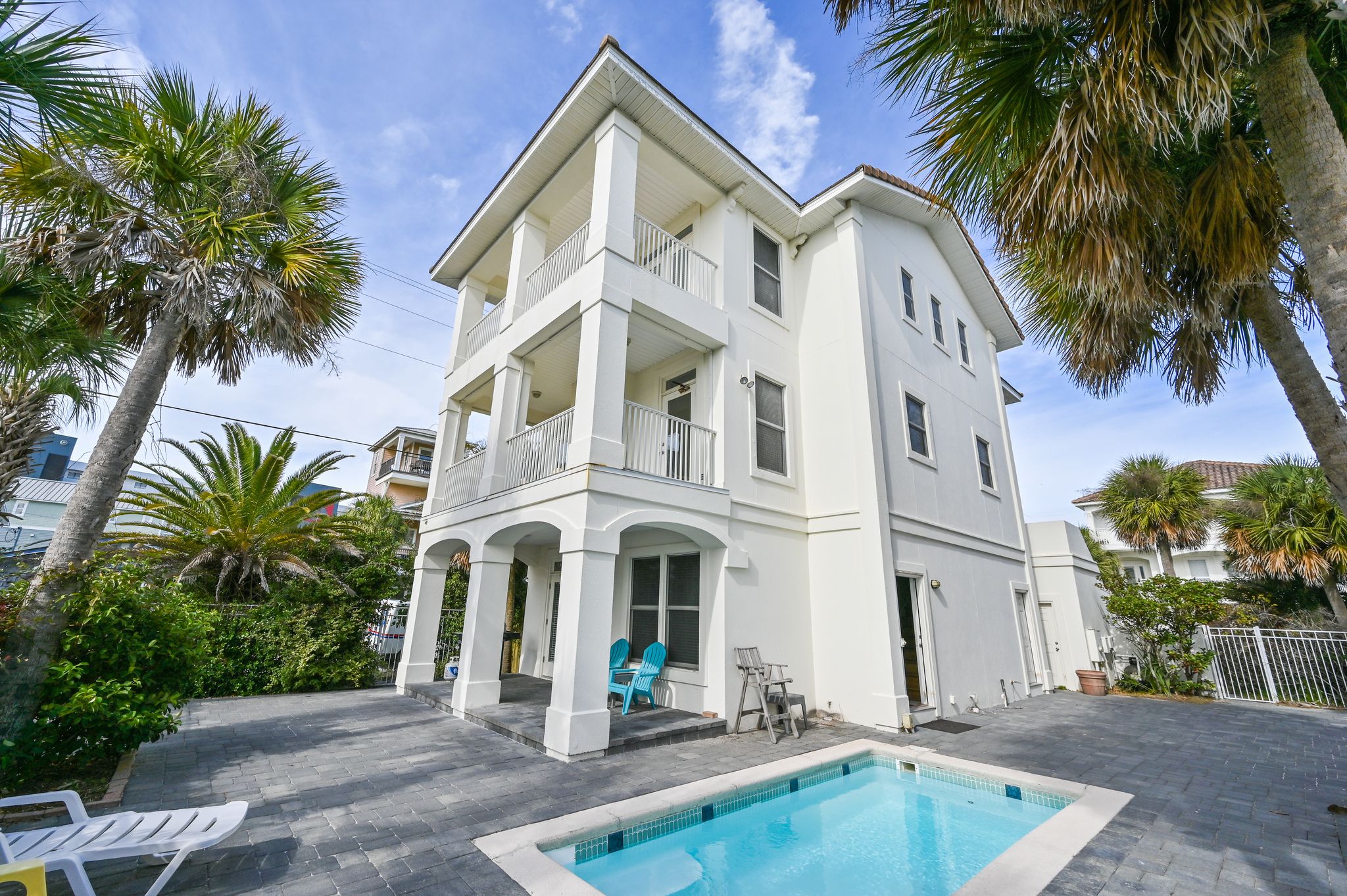 A two-story white building with a pool, surrounded by palm trees and a paved patio.
