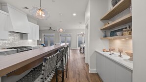 A modern kitchen with a long island, bar stools, pendant lighting, and a view to the dining area.