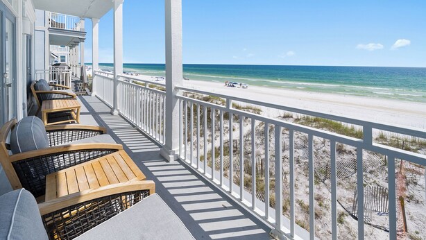 A balcony with wooden furniture overlooking a beach.