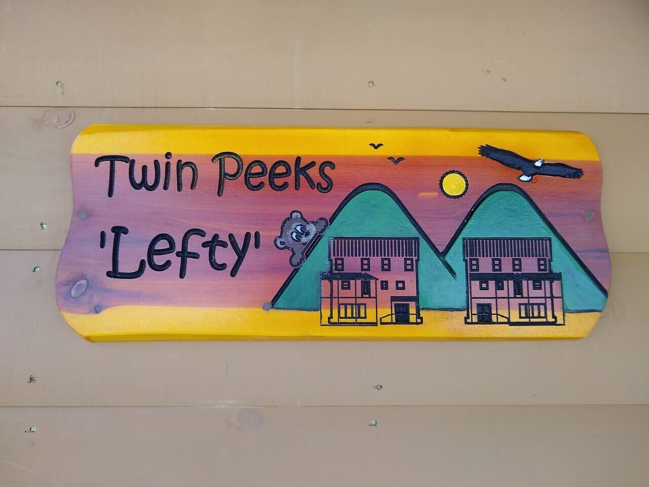 A wooden sign with 'Twin Peaks Lefty' and two buildings, a bird, and a sun.