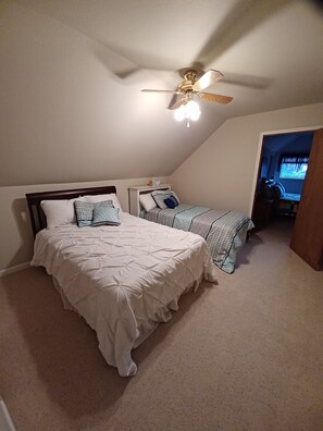 Une chambre avec deux lits, un ventilateur de plafond et une petite fenêtre.
