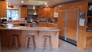 Una cocina moderna con armarios de madera, una isla central con taburetes, electrodomésticos de acero inoxidable y un amplio ventanal.