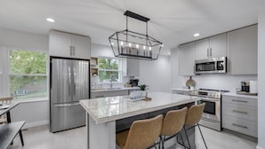 A modern kitchen with stainless steel appliances, a central island with bar stools, and white cabinetry. - Charming 4BR near Convention Ctr., Main St, & LU -just 11 minutes to STL Airport (Saint Charles)