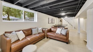 A modern living room with leather sofas, a coffee table, and a large window overlooking a residential area. - Charming 4BR near Convention Ctr., Main St, & LU -just 11 minutes to STL Airport (Saint Charles)