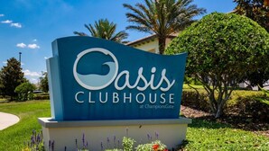 Señal de Oasis Clubhouse en ChampionsGate, con cielo despejado y vegetación de fondo.