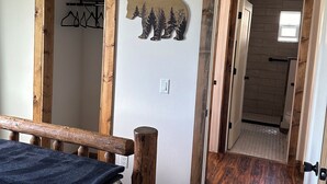 A bedroom with a wooden bed frame, a quilt, a coat rack, and a bear-shaped wall decoration.