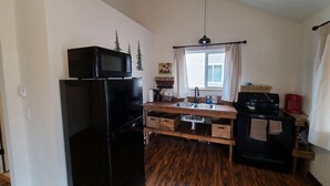 A compact kitchen with a black refrigerator, a wooden countertop, a sink, and a stove.